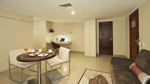A modern living room with a sofa, a dining table with chairs, and a kitchen area with cabinets and a laptop. - El Sol De Oro Hotel (Ollantaytambo)