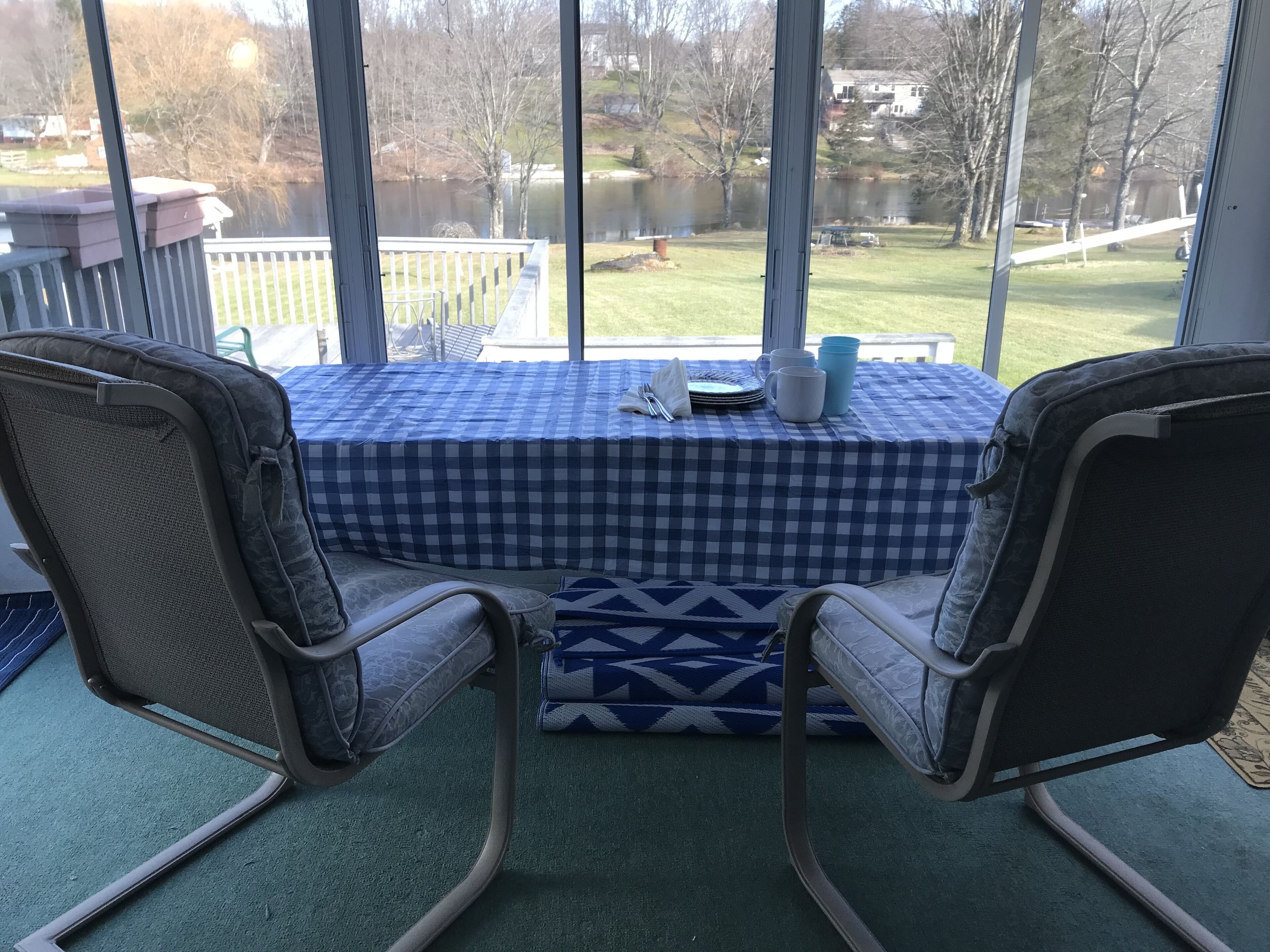 Une pièce avec deux fauteuils à bascule placés face à une table recouverte d’une nappe à carreaux, et offrant une vue sur un lac.
