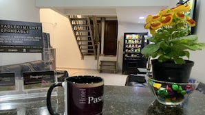 A hotel reception area with a marble counter, a 'Pasajero Suites' sign, a 'Hotel Pasajero' mug, a potted plant, and a vending machine.