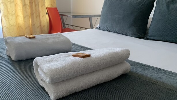 A neatly made bed with two folded white towels and a wooden bar.