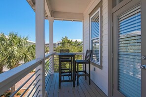 Un balcon abrité, doté d’une table et de chaises, qui offre une vue sur un quartier résidentiel avec des palmiers et des maisons.