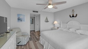 Un dormitorio con cama, ventilador de techo, mesita de noche con lámpara, televisor y cómoda.