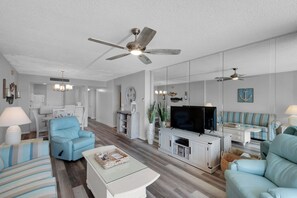 A modern living room with a ceiling fan, a flat-screen TV, and light blue sofas. - Dunes Of Panama B208 (Panama City Beach)