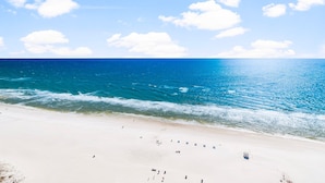 Ein Strand mit klarem, blauem Wasser, einem Sandstrand und einigen Personen sowie Sonnenschirmen.