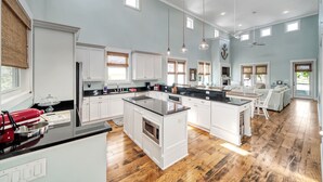 A spacious kitchen with white cabinetry, a large island, and a dining area with a white table and chairs. - Windmark Beach House | Walk to Beach | Pool & Pets (Port St Joe)