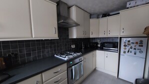 Une cuisine avec des meubles blancs, un plan de travail noir, une cuisinière à gaz, un four, un four à micro-ondes et un réfrigérateur.