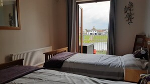 Une chambre avec deux lits, une fenêtre donnant sur des immeubles, un radiateur et une plante fixée au mur.