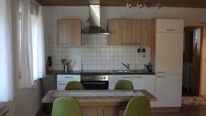 Een keuken met houten kastjes, een betegelde achterwand, een fornuis en twee groene stoelen.