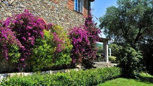 Un edificio de piedra con un jardín que presenta vibrantes buganvillas rosadas.