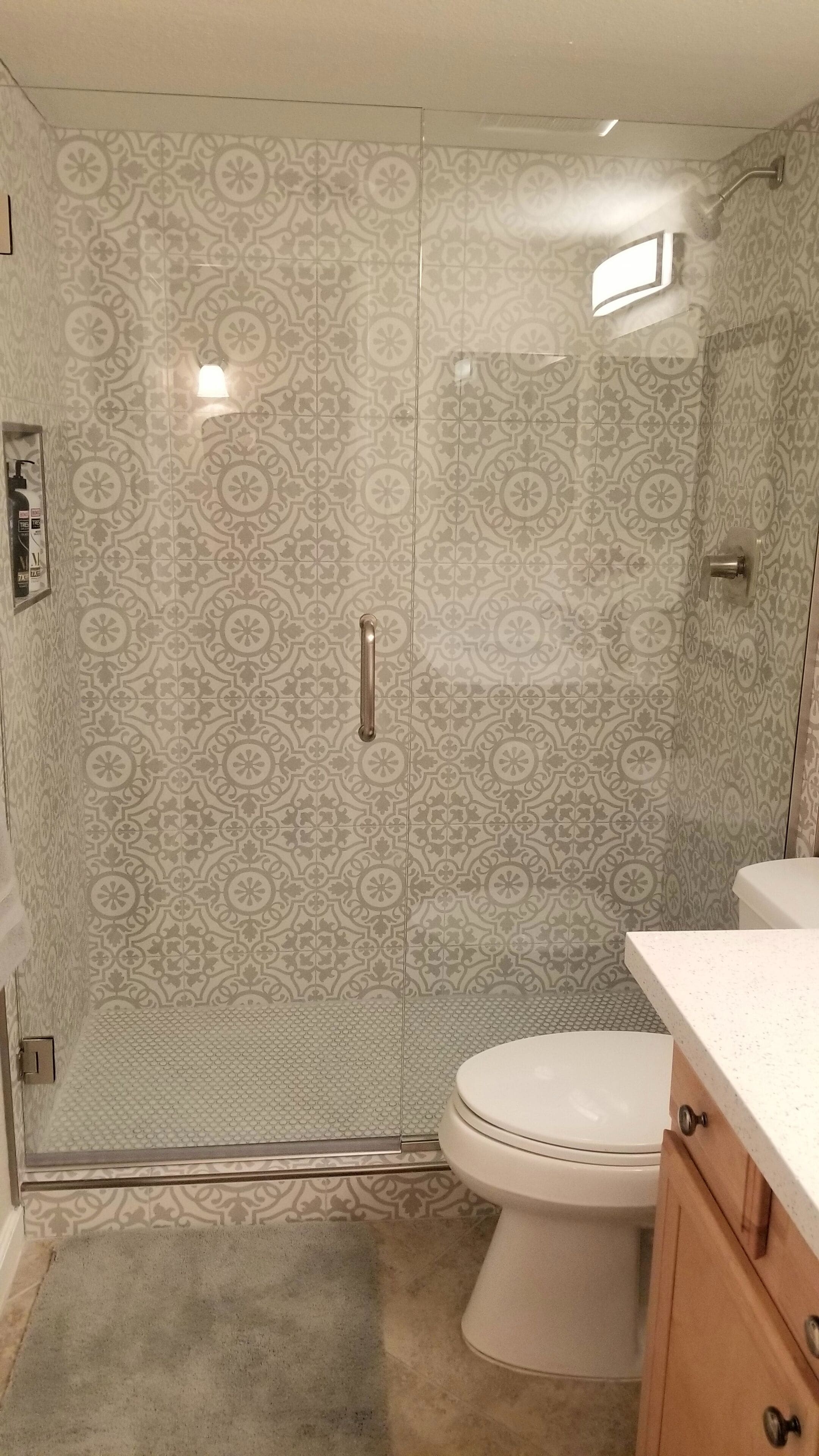 A bathroom with a patterned tile wall, a glass shower enclosure, a toilet, and a countertop with a sink.