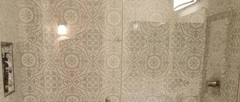 A bathroom with a patterned tile wall, a glass shower enclosure, a toilet, and a countertop with a sink.
