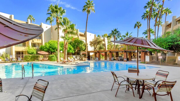 A swimming pool with lounge chairs and umbrellas, surrounded by palm trees and a building with balconies. - Home At The Maya.... (Scottsdale)