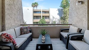 A balcony with wicker furniture, a potted plant, and a view of a building with palm trees. - Home At The Maya.... (Scottsdale)