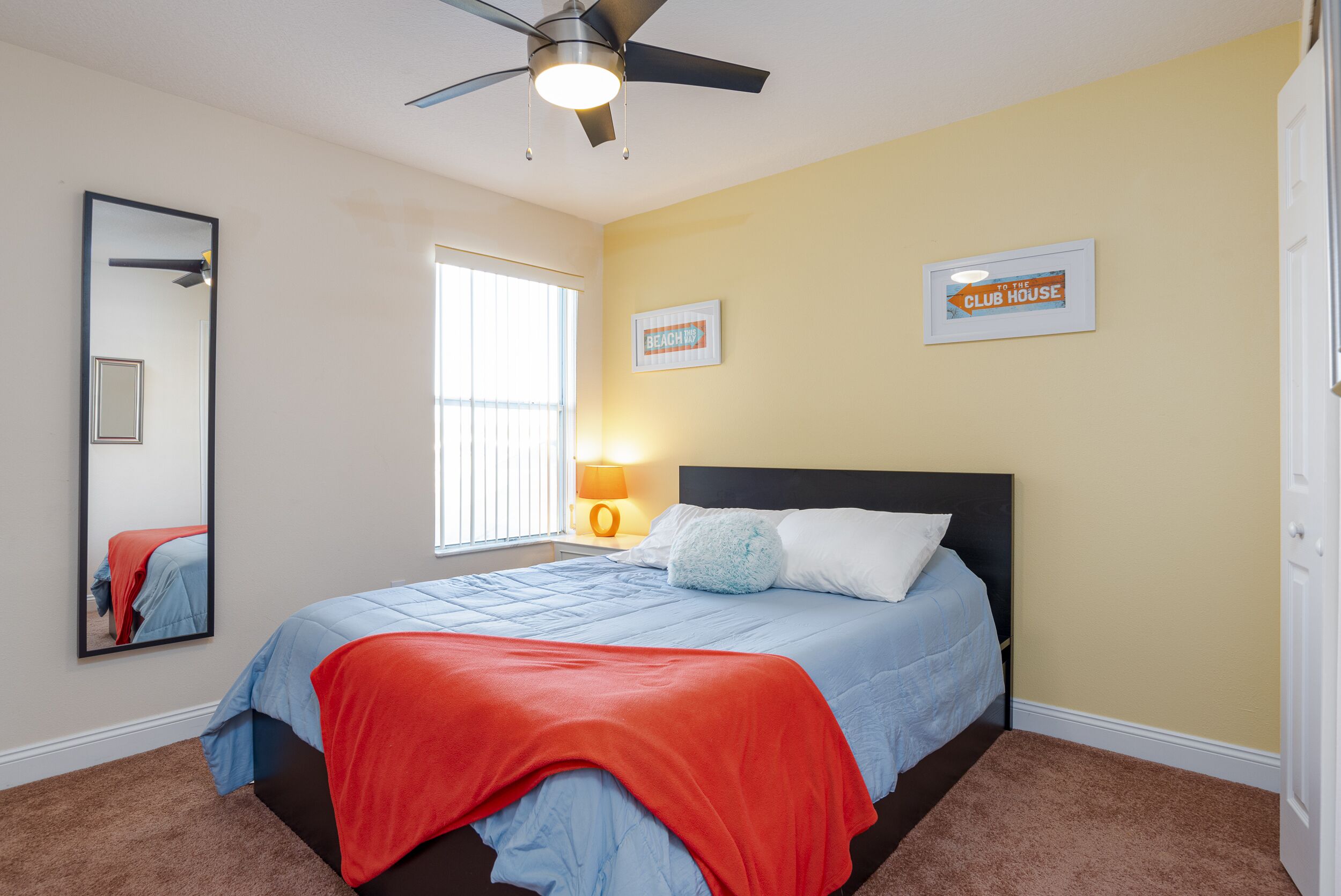 A bedroom with a bed, a ceiling fan, a window, and two wall-mounted signs.