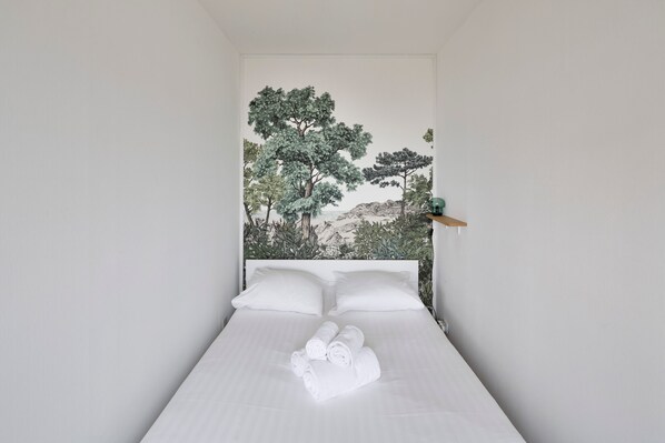 Una cama bien tendida con toallas blancas enrolladas en una habitación con un mural de árboles y montañas en la pared.