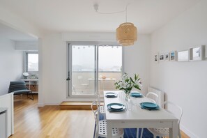 Un comedor moderno con una mesa blanca para cuatro, platos azules y una lámpara colgante tejida.