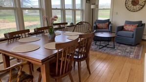 Een eetgedeelte met een houten tafel en stoelen, een vaas met bloemen en uitzicht door grote ramen.