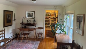 Een gezellige kamer met een houten eettafel, stoelen, een boekenkast en een groot raam.