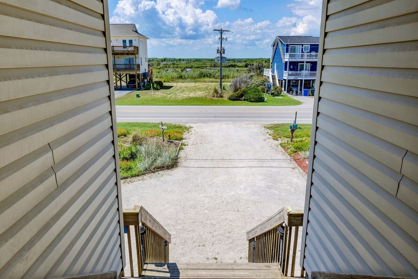 A view from a window overlooking a driveway leading to a house with a deck and a grassy area.