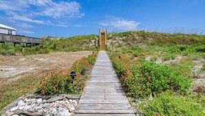 A wooden boardwalk leading to a structure with a wooden facade, surrounded by a natural landscape with grasses and wildflowers. - 3800 Island Drive- Pet Friendly, Direct Oceanfront with Amazing Oceanview's from 2 decks- Adjoini... (North Topsail Beach)