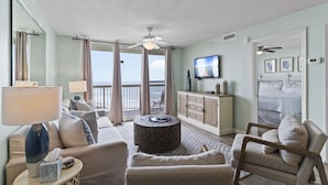 A hotel room with a balcony, a television, a bed, and a seating area with a lamp and a side table.