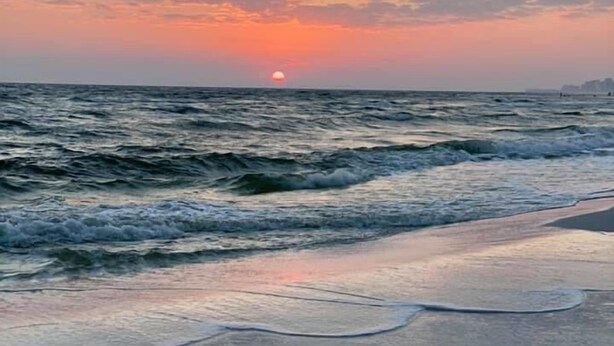 A beach with waves and a sunset.