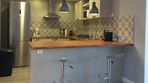Moderni keittiö, jossa on ruostumattomasta teräksestä valmistettu jääkaappi, puinen työtaso, kaksi baarituolia ja riippuvalaisimet.