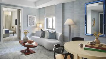 Ein modernes Wohnzimmer mit grauem Sofa, rundem Couchtisch und Esstisch mit Stühlen. An der Wand hängt ein großer Spiegel und ein Fenster mit Jalousien.