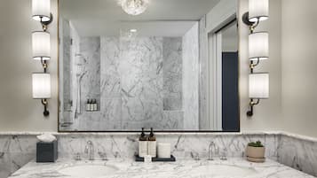 A bathroom with two sinks, marble walls, a large mirror, and wall-mounted lighting.