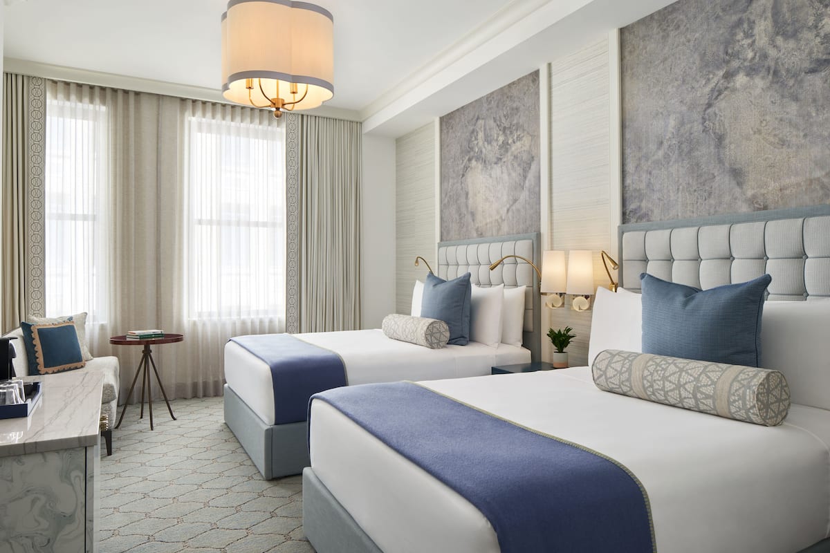 A hotel room with two beds, a desk, and a large window with curtains.