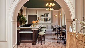 A bar area with a marble countertop, cushioned stools, and a chandelier. - The Wall Street Hotel (New York)