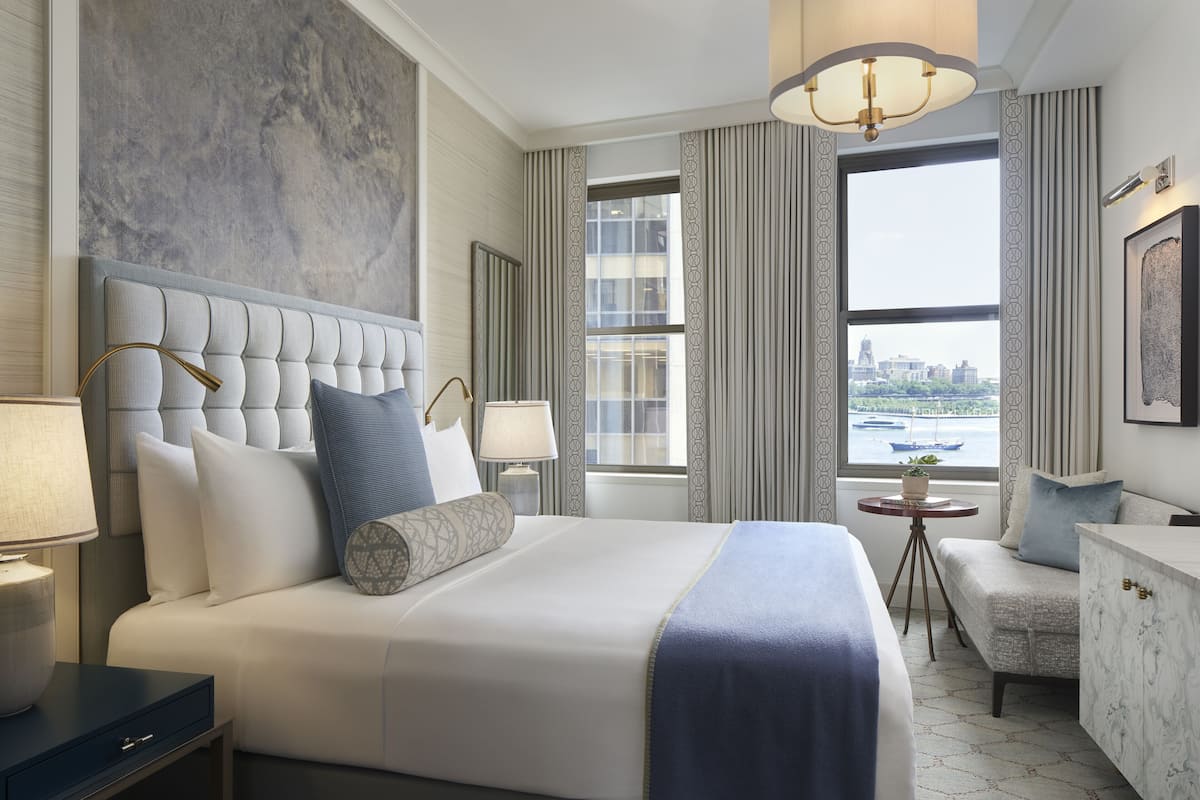 A hotel room with a large bed, a desk, a chair, a small table, and a view of the city through the window.