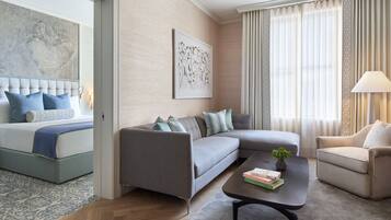 A modern hotel room with a bed, grey sofa, armchair, and a coffee table with books.