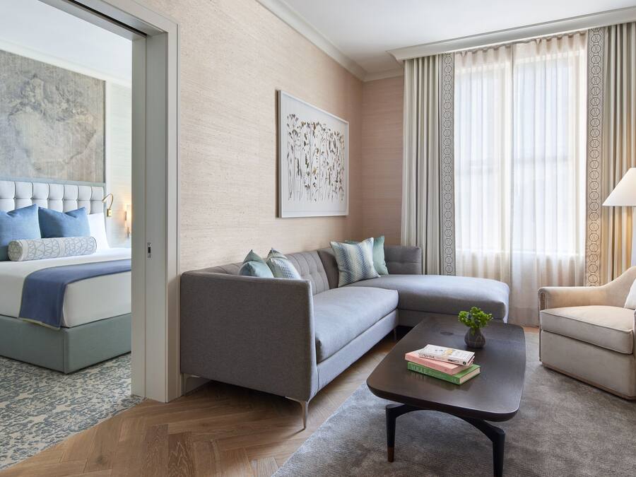 A modern hotel room with a bed, grey sofa, armchair, and a coffee table with books.