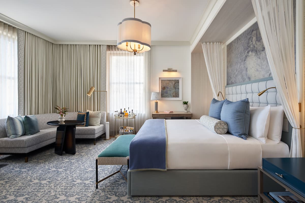 A hotel room with a large bed, a sofa, a small table, and a nightstand.