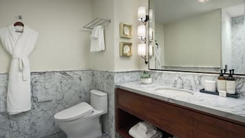 A bathroom with a marble wall, a white toilet, a vanity with a mirror, and a robe hanging on the wall.