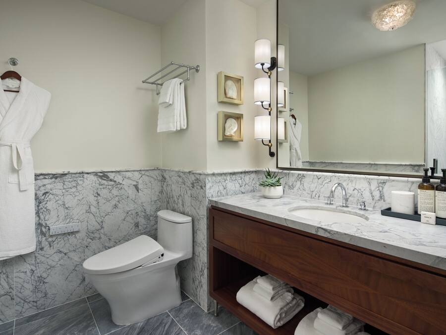 A bathroom with a marble wall, a white toilet, a vanity with a mirror, and a robe hanging on the wall.