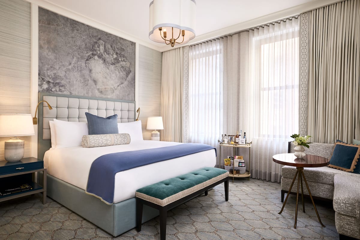 A hotel room with a large bed, a bench, a small table, and a sofa.