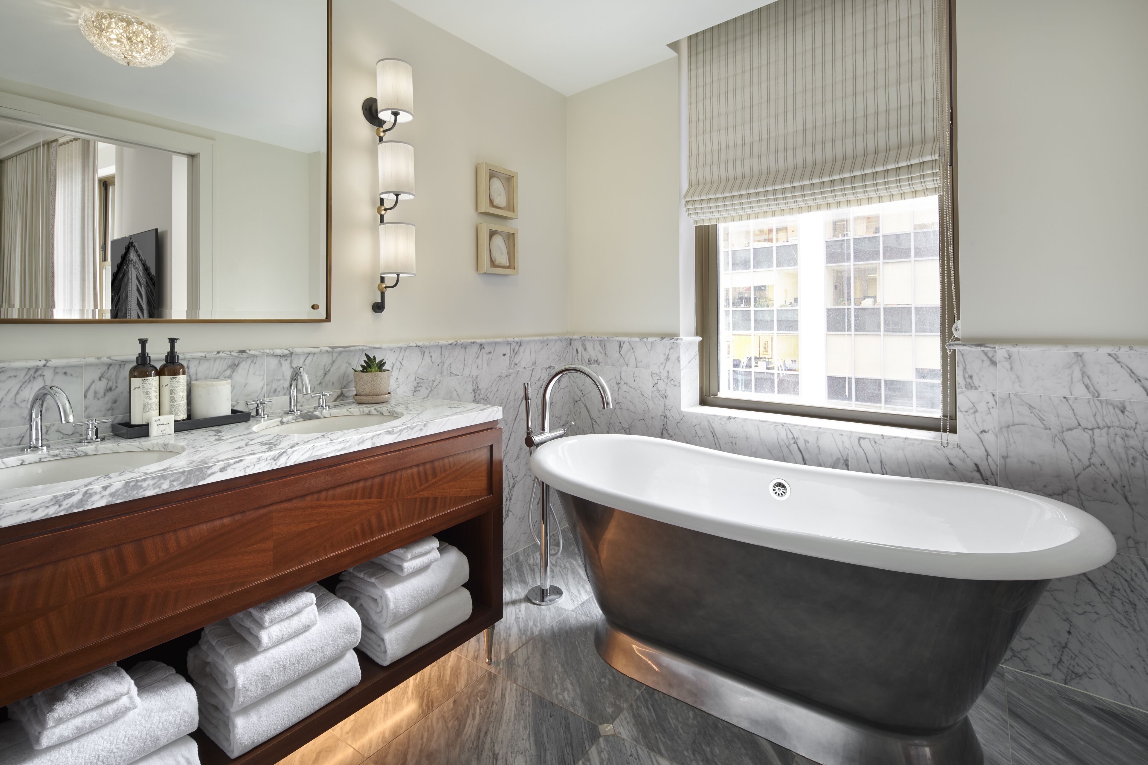 A bathroom with a freestanding bathtub, marble countertops, a wooden vanity, and a large mirror.