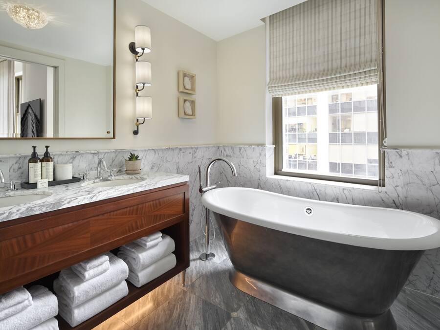 A bathroom with a freestanding bathtub, marble countertops, a wooden vanity, and a large mirror.