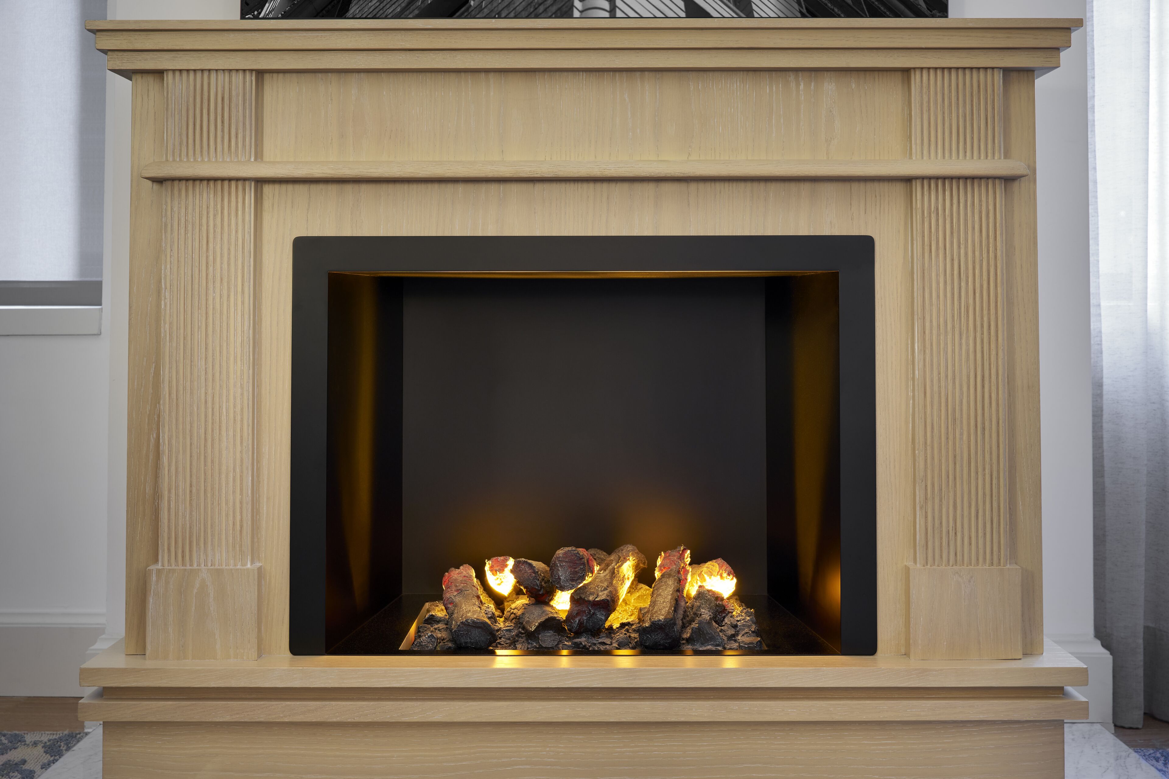 A fireplace with a wooden mantel and a fire burning inside.