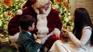 A person in a Santa suit seated on a stool with a child and a woman.