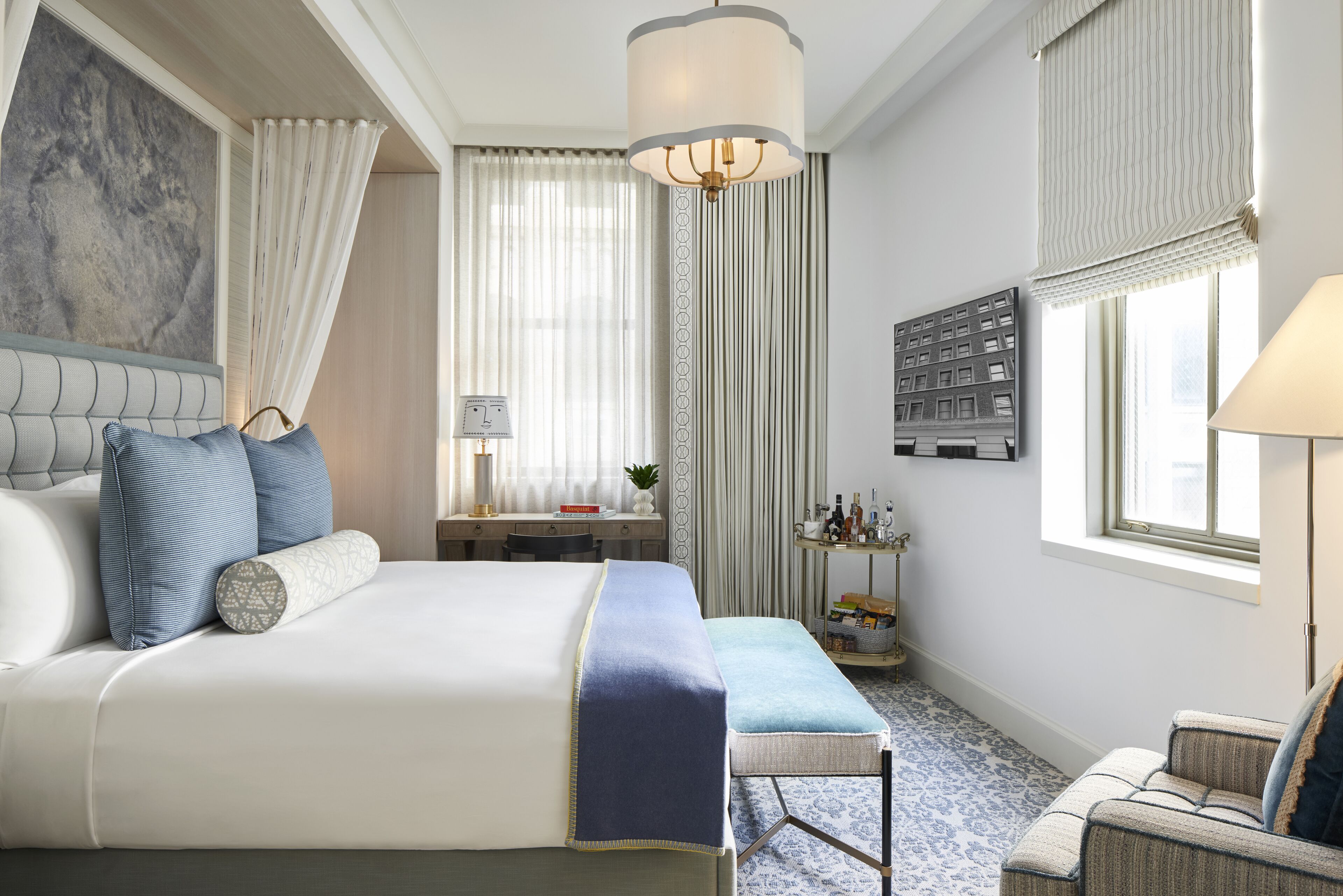A hotel room with a large bed, a desk, a chair, a lamp, and a window with curtains.