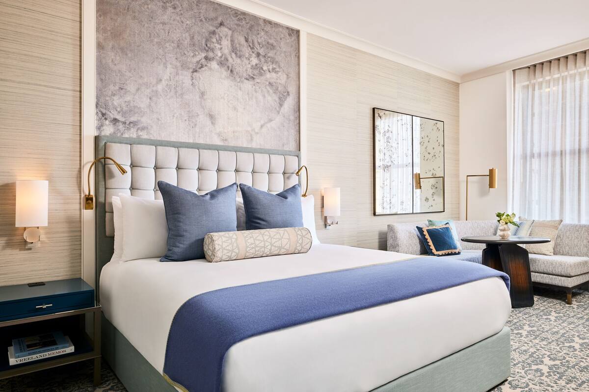 A hotel room with a large bed, a sofa, a small table, and a nightstand.