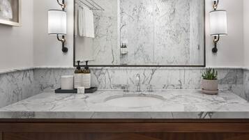 A modern bathroom with a marble countertop, a large mirror, wall-mounted sconces, and a towel rack.