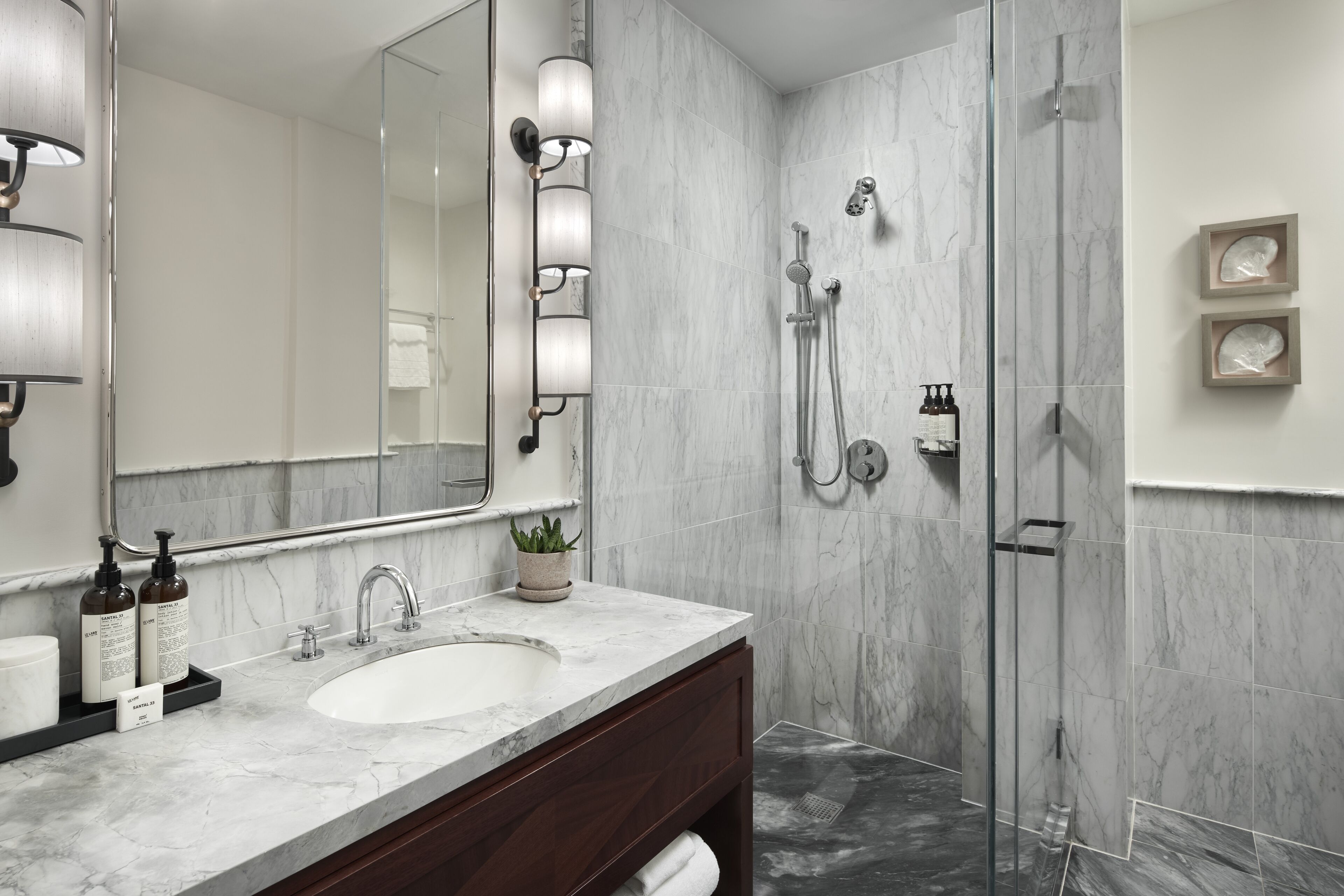 A modern bathroom with a marble sink, a large mirror, and a glass-enclosed shower.