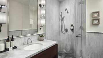 A modern bathroom with a marble sink, a large mirror, and a glass-enclosed shower.