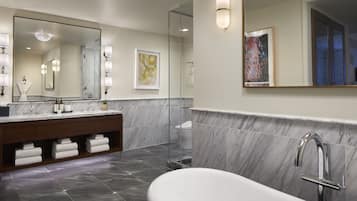 Een moderne badkamer met een grote spiegel, een vrijstaand bad en een douchegedeelte betegeld met marmer.