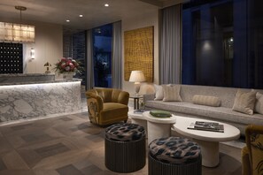 Un moderno vestíbulo de hotel con un mostrador de recepción de mármol, un sofá, pufs y una mesa de centro.