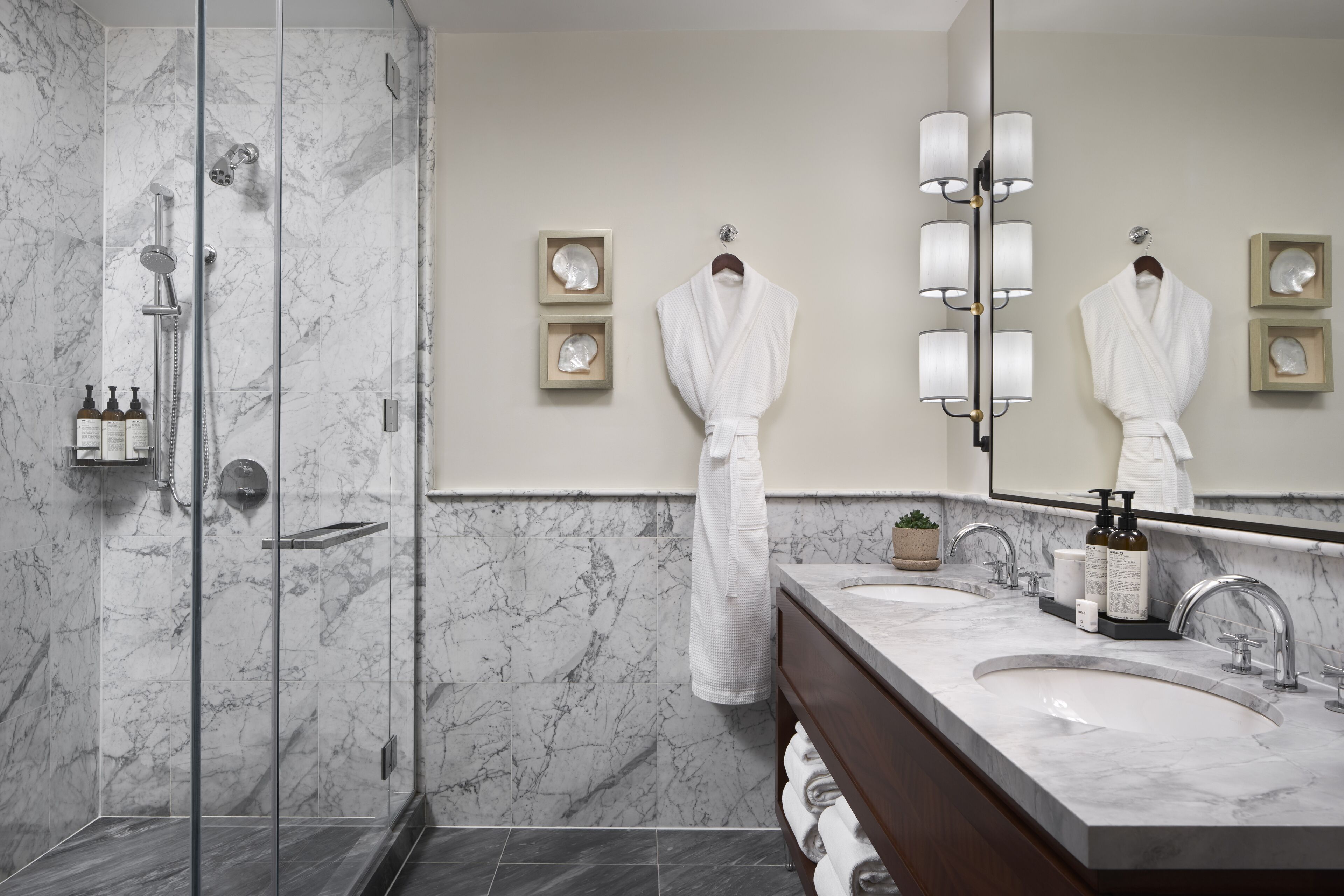 Un baño moderno con cabina de ducha de vidrio, paredes de mármol, un espejo grande y tocador con lavabo y perchero para toallas.